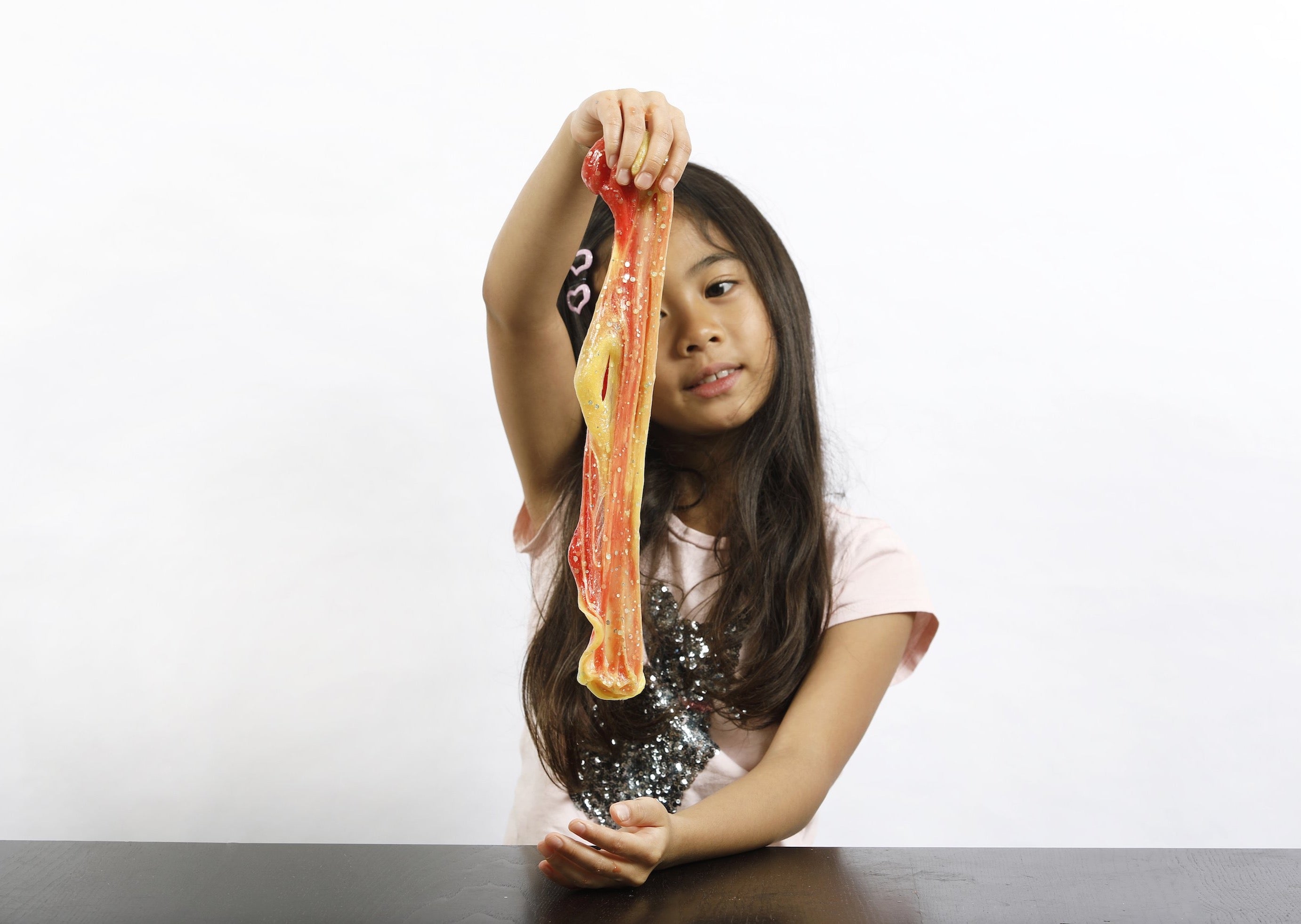 Young girl stretching orange and yellow color-changing Sunset slime.