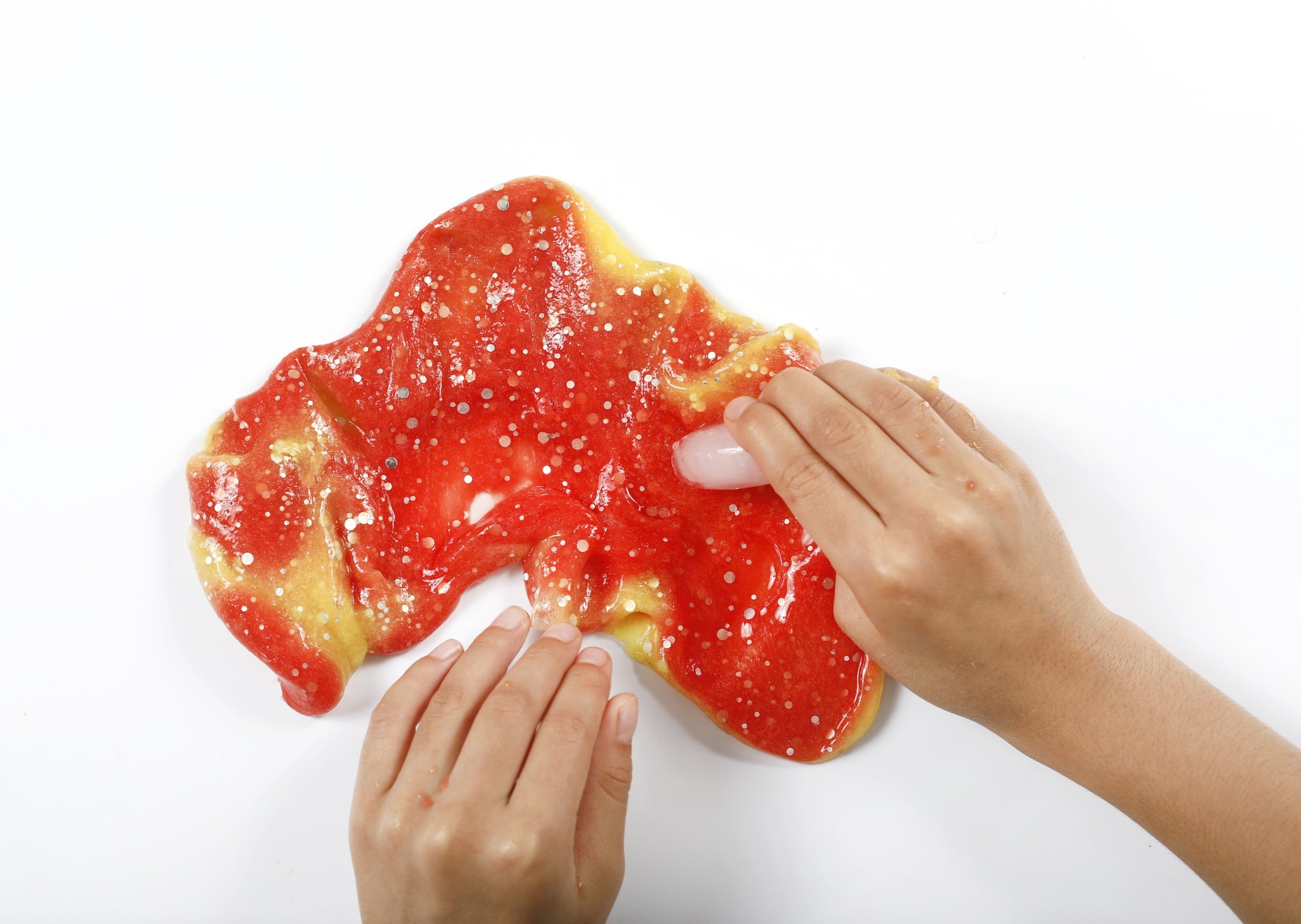 Two hands running an ice cube over Sunset slime to change it from orange to yellow based on temperature.