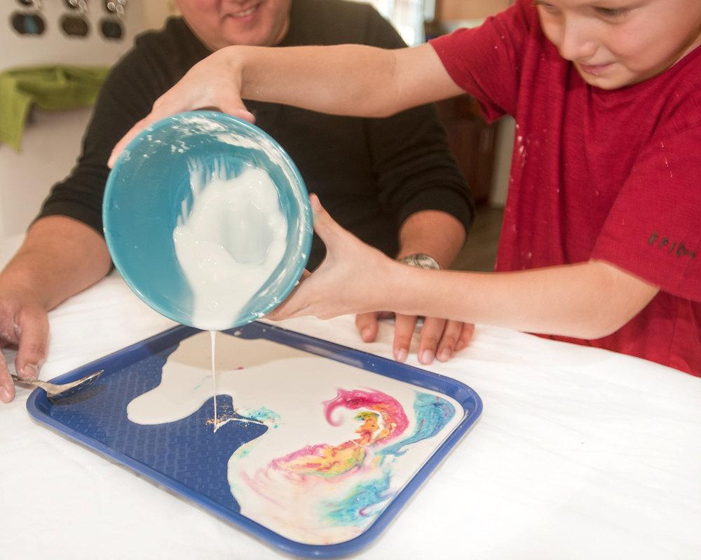 Child pouring a mix of white and colorful material onto a tray.