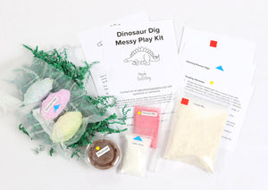 Materials and contents of Dinosaur Dig Messy Play Kit including instructions, dinosaur eggs, play dough, volcano mix, citric acid, and fossil mix.