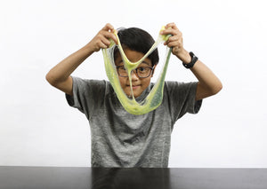 Young boy wearing glasses stretching green and yellow color-changing Caterpillar slime in front of his face.