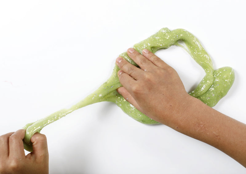 Two hands pulling apart a ring of stretched and folded green Caterpillar slime.