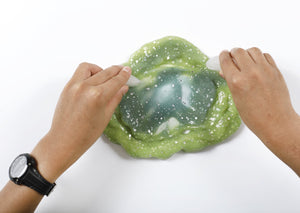 Two hands running ice cubes along a ring of stretched and folded Caterpillar slime to change its color.