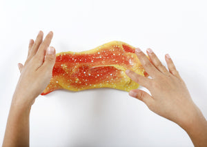 Two hands playing with Messy Play Kit's color-changing Sunset slime with thermochromic pigment that changes from orange to yellow based on temperature.