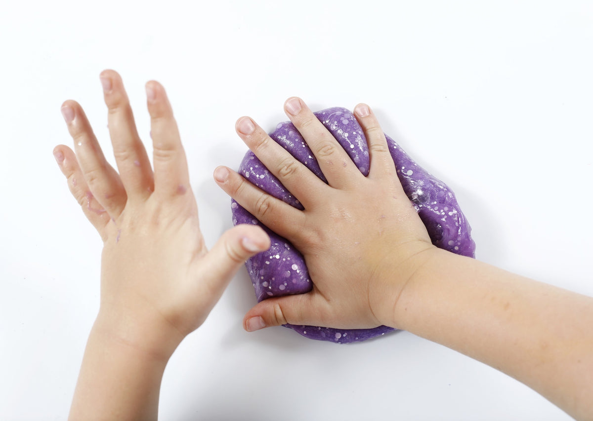 Child's hands pushing into a ball of purple Rockstar slime from Messy Play Kits.