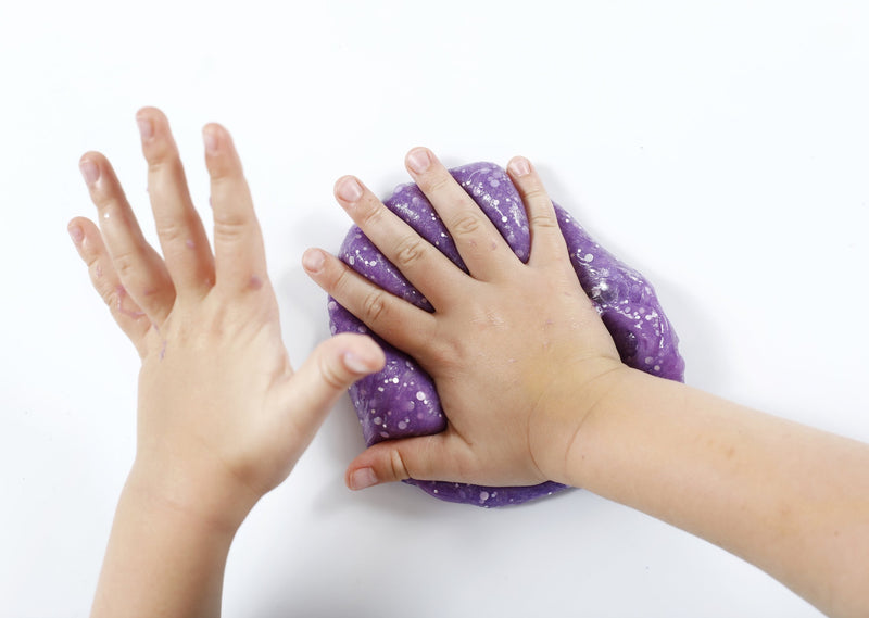 Child's hands pressing into purple glitter slime making an imprint.