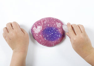 Child's hands running an ice cube along a ball of warmed up Rockstar slime to change its color from pink back to purple.