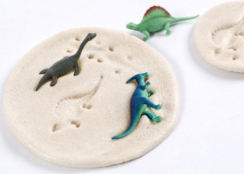 Close up of toy dinosaurs in dough, showing imprints that look like dinosaur fossils.