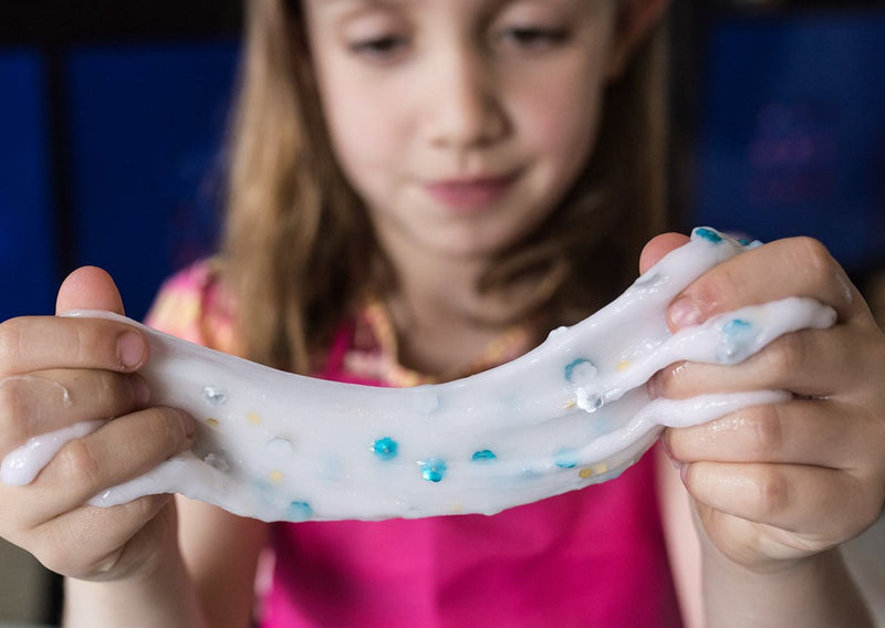Girl stretching white slime with blue sequins between her hands.