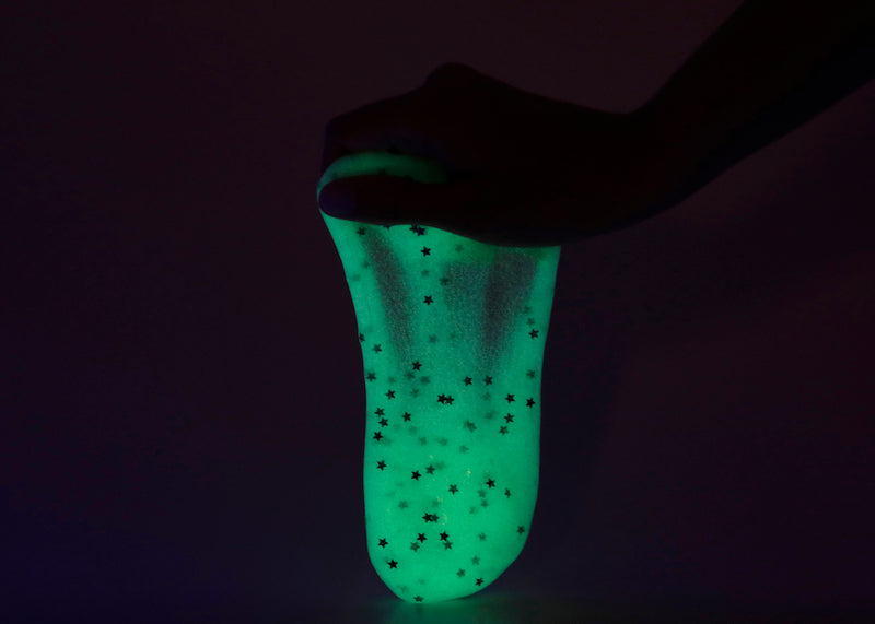 Hand holding Messy Play Kit's glow-in-the-dark slime in a dark room.