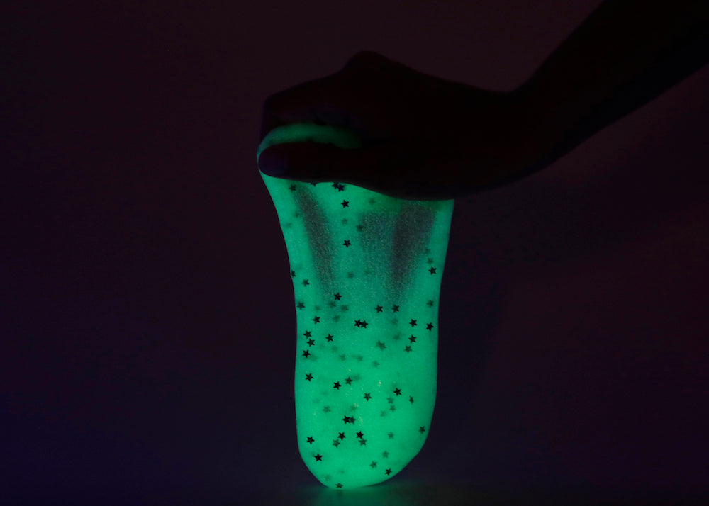 Hand holding Messy Play Kit's glow-in-the-dark slime in a dark room.