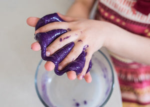 Child's hands playing with purple slime over a bowl.