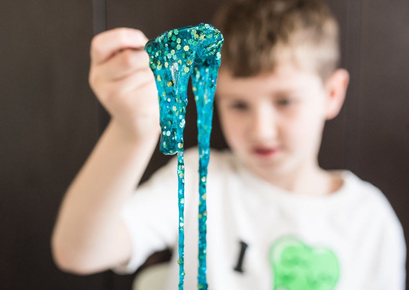 Boy lifting turquoise sequin slime up with a spoon.