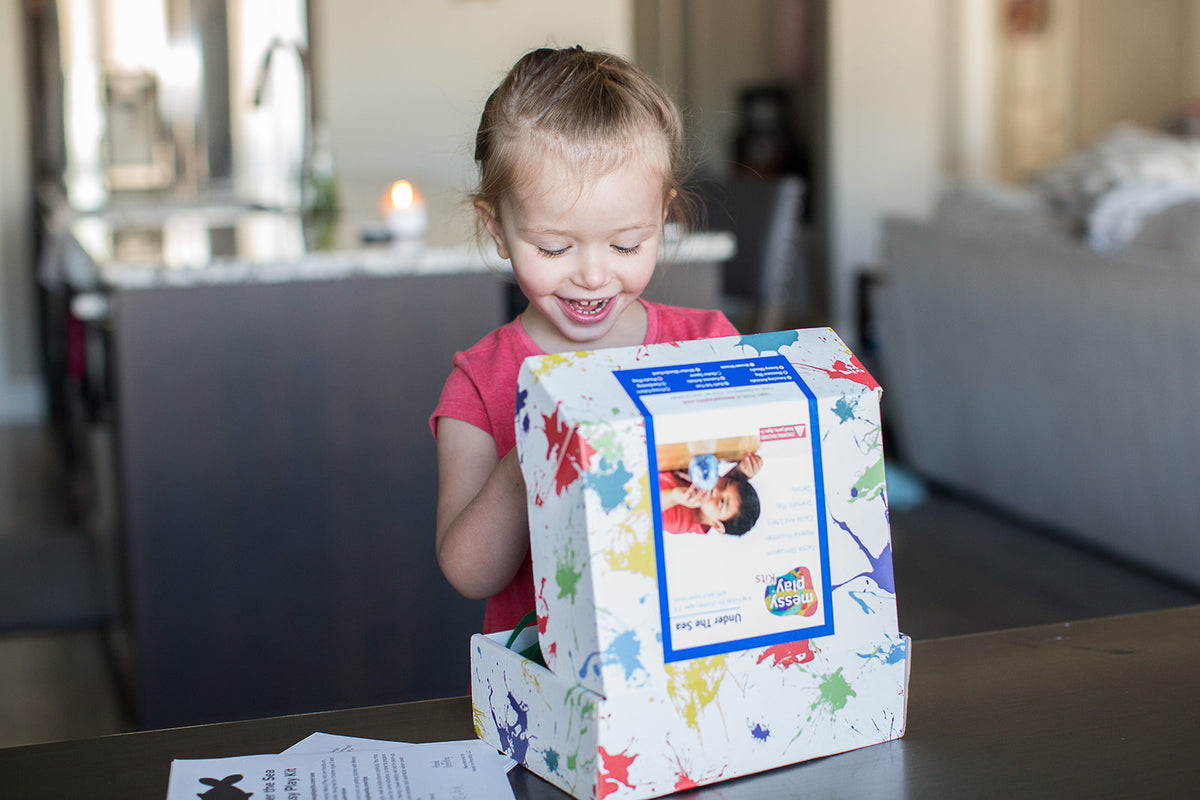 An excited girl opening her "Under the Sea" themed STEM subscription box from Messy Play Kits