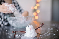 A child's hand using a pipette to drop citric acid onto a snowman made of baking soda paste for the Fizzing Snowman activity from the Winter Wonderland kit