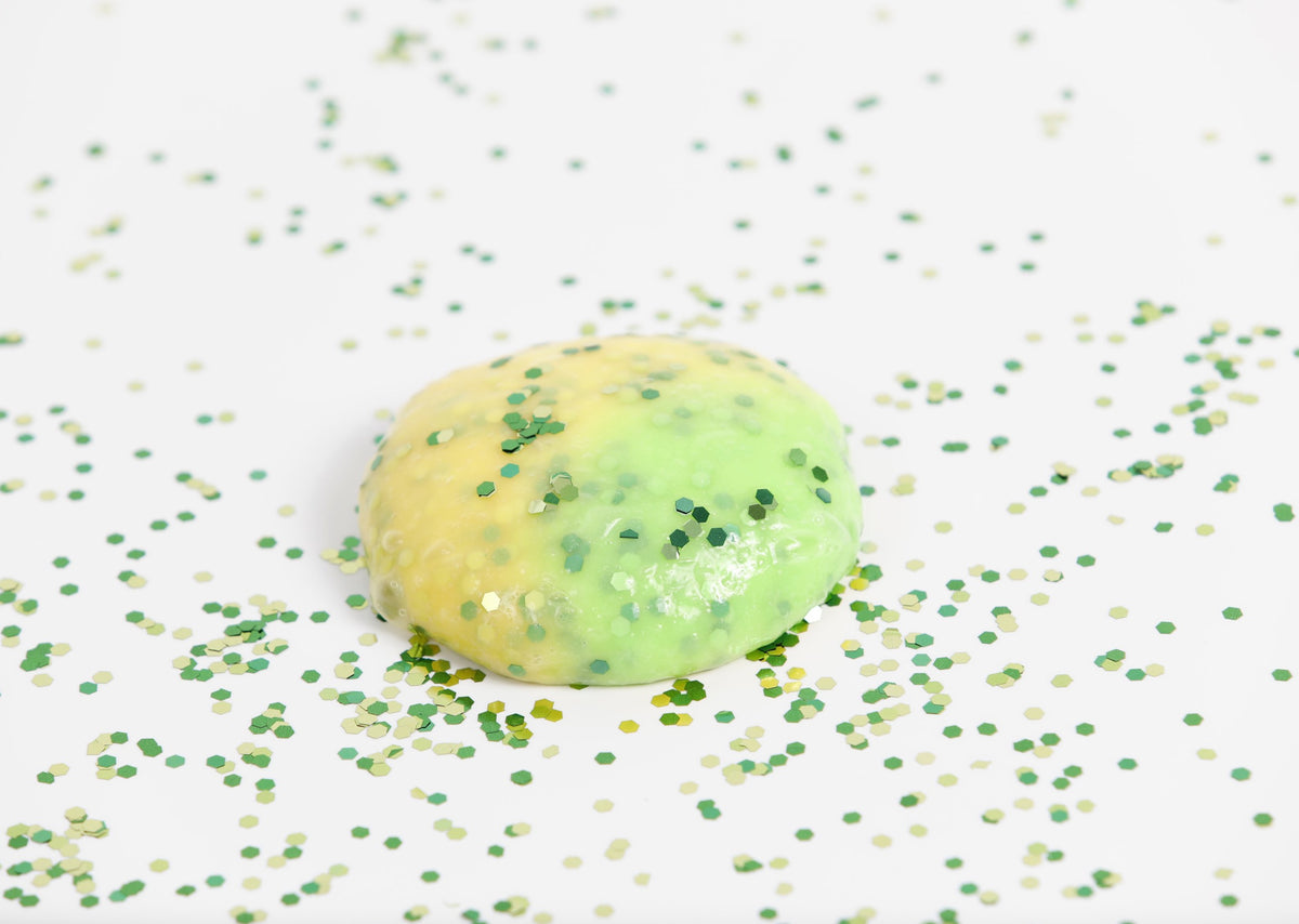 Glitter surrounding a round ball of Messy Play Kit's Dragon color-changing slime that changes from yellow to green in the sunlight