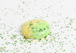 Glitter surrounding a round ball of Messy Play Kit's Dragon color-changing slime that changes from yellow to green in the sunlight