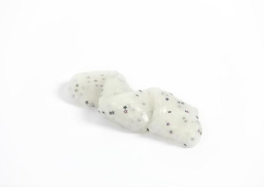 Stretched and folded white Glow in the Dark slime with glitter stars laying on a table in a bright room.