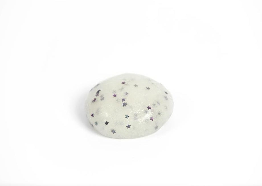 A ball of Messy Play Kit's glow-in-the-dark slime in a bright room. Slime is white with glitter stars.