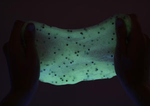 Two hands in a dark room pulling and stretching the Glow in the Dark slime revealing the glitter stars.