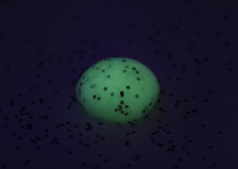 A ball of Messy Play Kit's glow-in-the-dark slime glowing in a dark room.