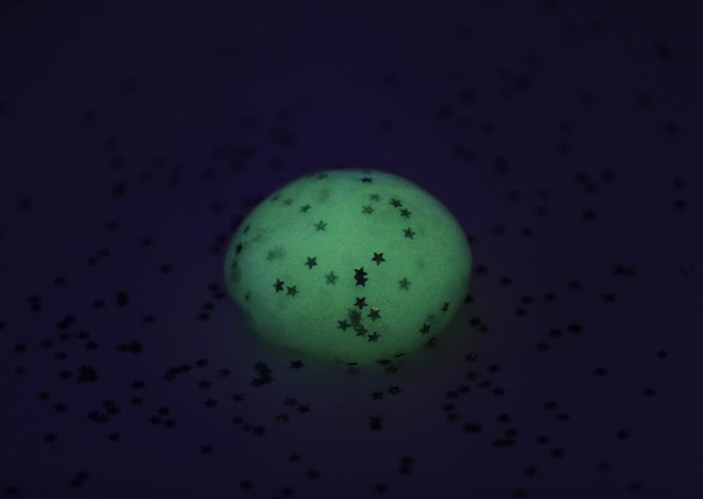 A ball of Messy Play Kit's glow-in-the-dark slime glowing in a dark room.