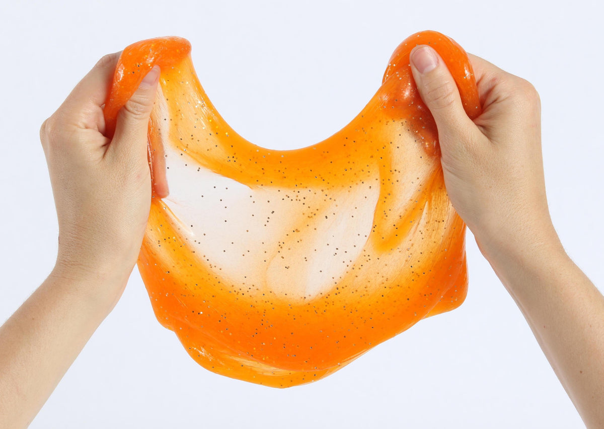Two hands pulling and stretching the orange glitter slime by Messy Play Kits.