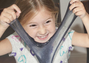 Young girl smiling while stretching slime in front of her face.