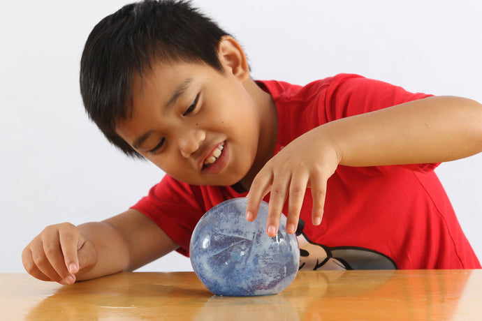 Boy examining round ball of ice in the density experiment in the Under the Sea Messy Play Kit,