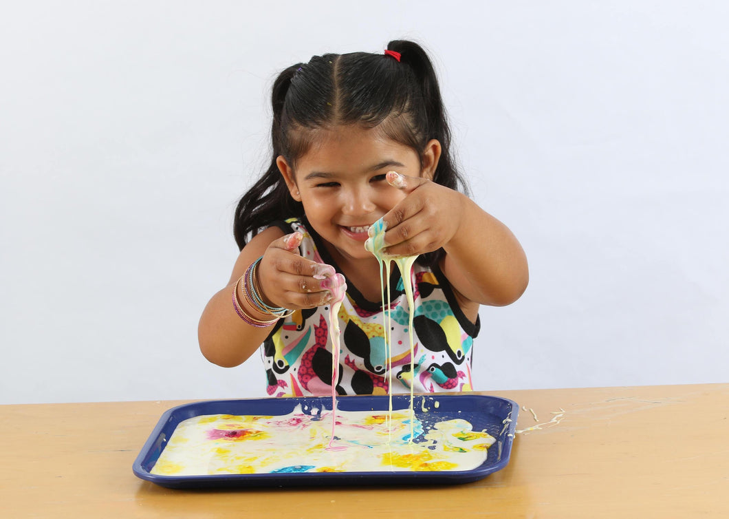 Smiling girl dipping her hands in colorful ooze from the colorburst oobleck activity.