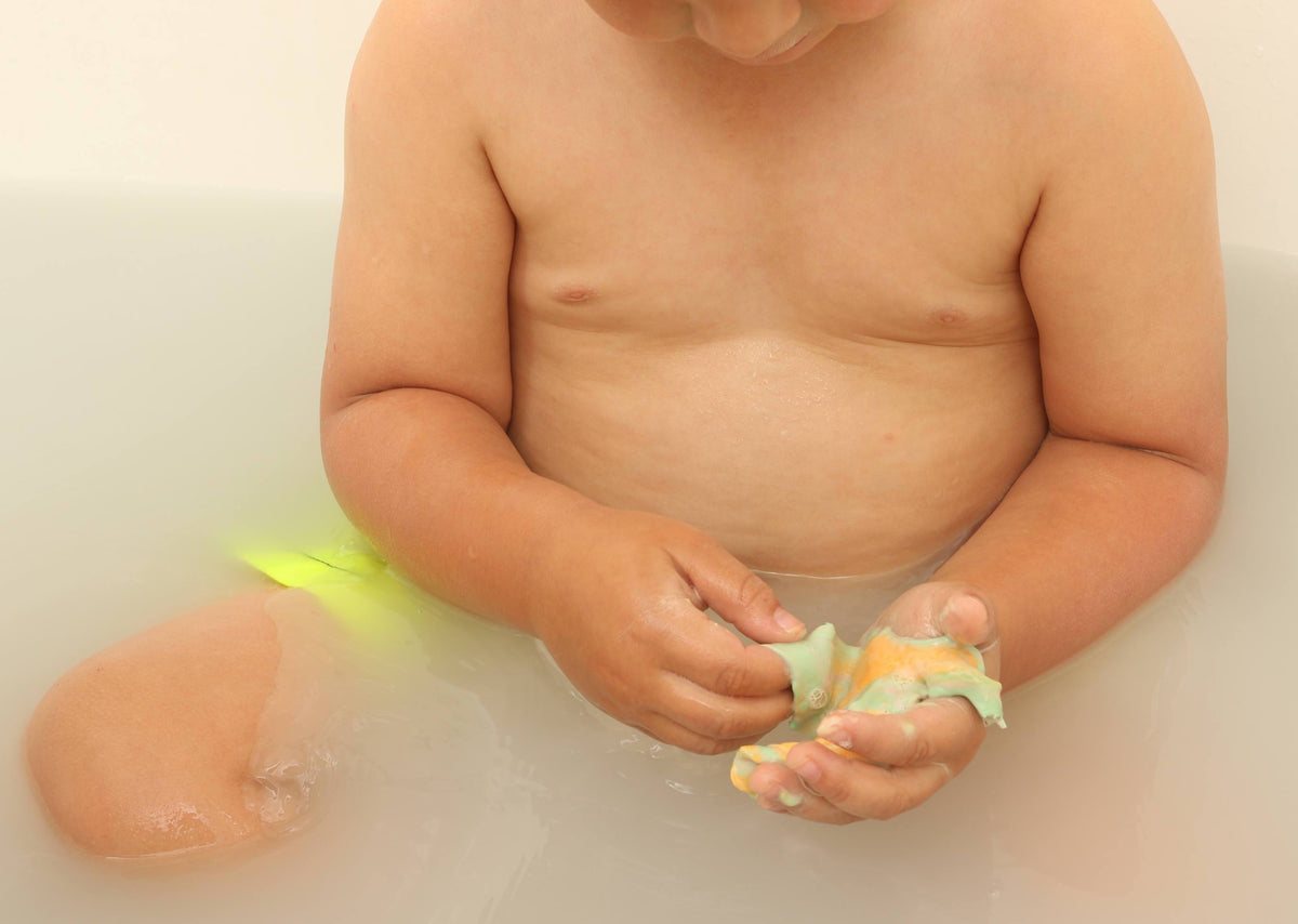 Child playing and molding green playdough soap in his hands in the bathtub.
