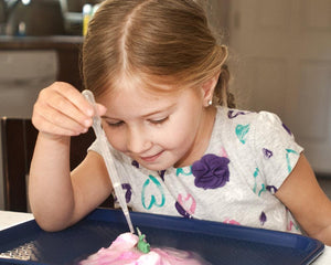 Girl using a pipette to drip liquid onto a dinosaur egg to make it hatch a toy dinosaur.