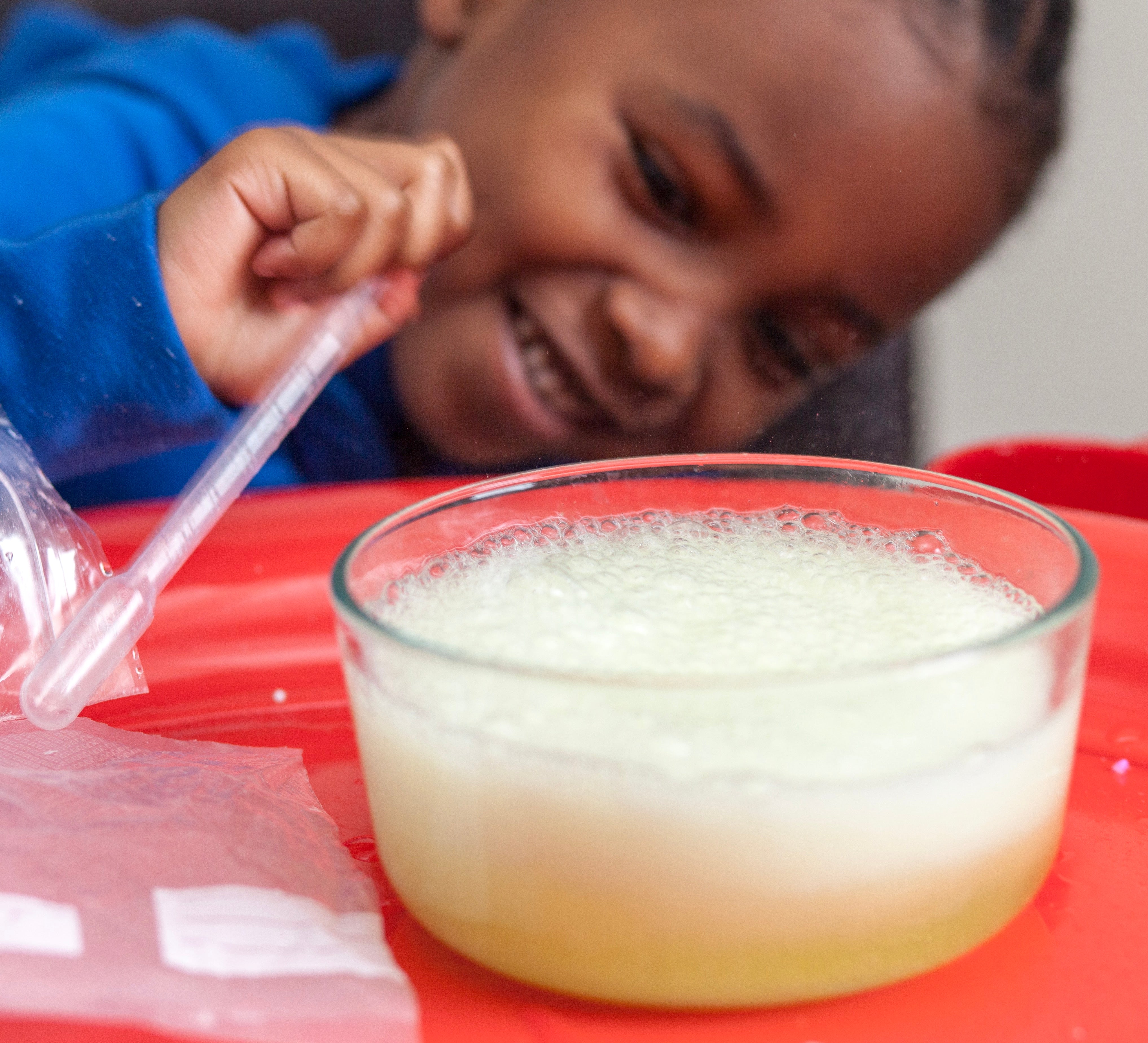 Child holding a pipette while looking at a bowl of bubbly liquid from his kids science subscription box kit