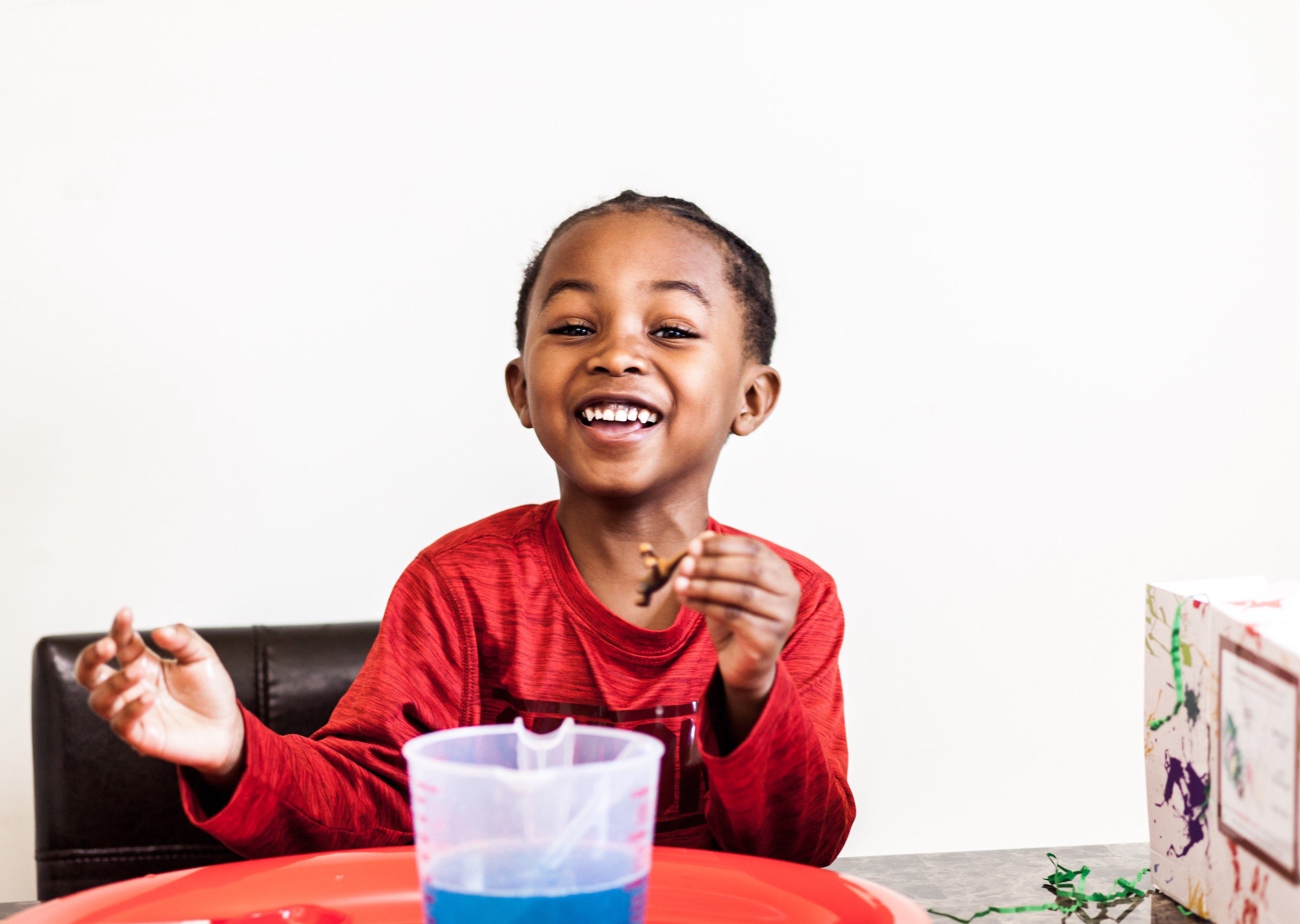 Boy laughing while holding a toy dinosaur next to his Dinosaur Dig Messy Play Kit supplies.