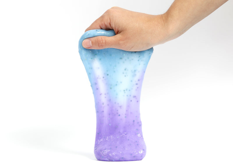 Hand holding Messy Play Kit's color-changing Mermaid slime that changes from blue to purple in the sunlight