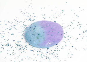 Glitter surrounded a round ball of Mermaid slime that changes from blue to purple in the sunlight