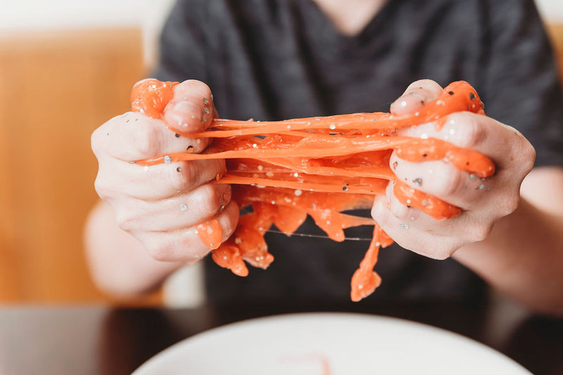 A kid's hands squeezing and stretching an orange slime